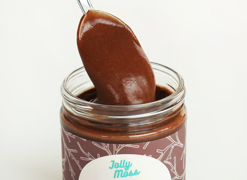 Spoon lifting a portion of chocolate sea moss pudding from a jar labeled 'Jolly Moss'